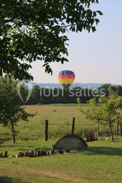Montgolfière colorée flottant au-dessus d'un champ verdoyant avec des arbres et une clôture en bois au premier plan.