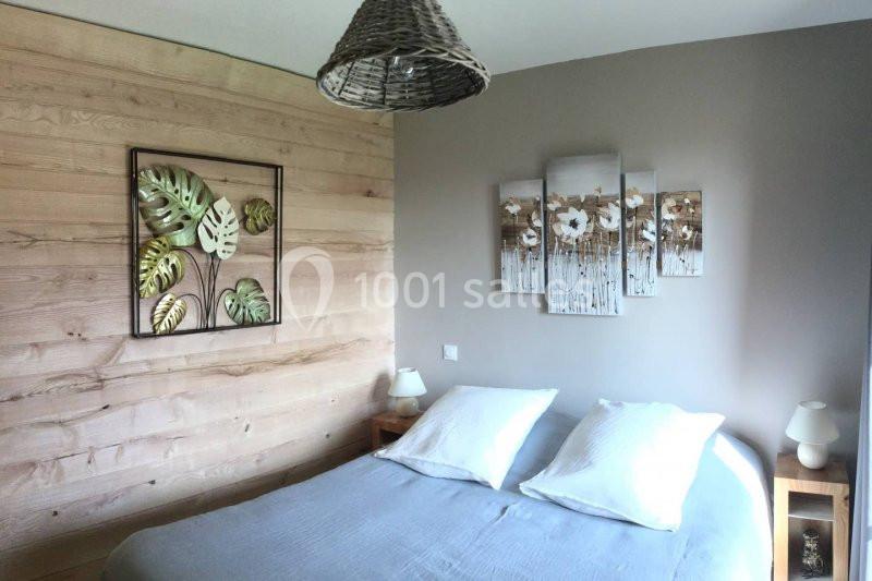 Chambre avec lit double, mur en bois, décoration murale végétale et luminaires en osier et céramique.