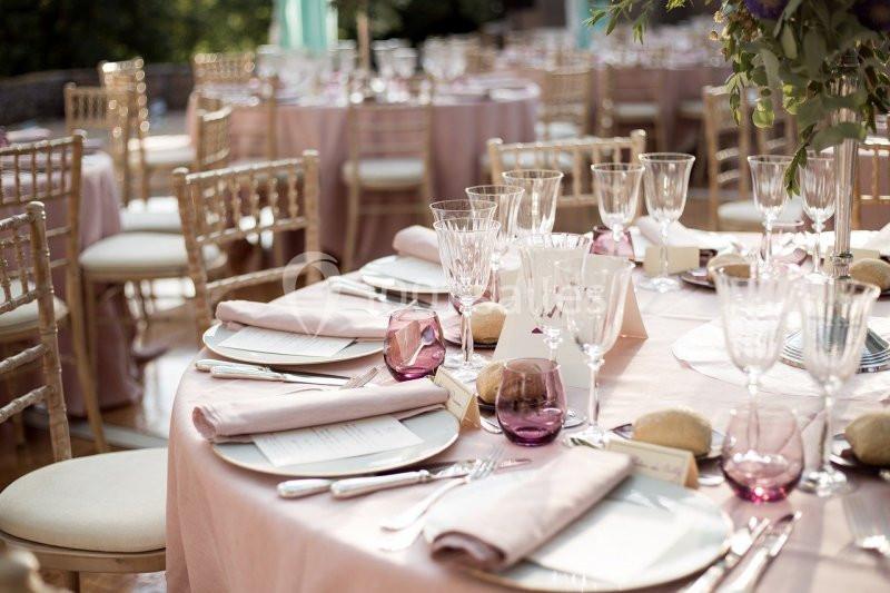 Tables élégamment dressées avec nappes roses, verres en cristal, serviettes pliées et chaises en bois clair.