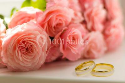 Bouquet de roses roses posé sur une surface blanche avec deux alliances dorées au premier plan.