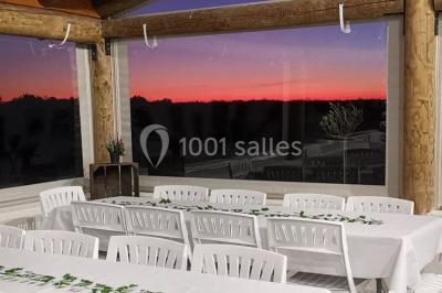 Maison blanche aux volets bleus éclairée la nuit, entourée d'arbres et d'une pelouse.