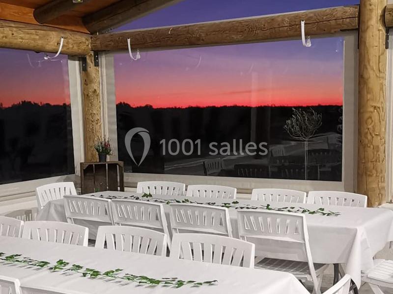 Salle de réception avec tables blanches décorées de feuillage, offrant une vue sur un coucher de soleil coloré.