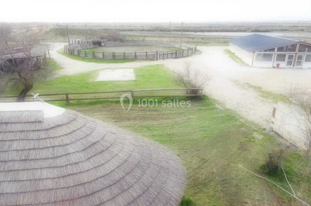 Vue aérienne d'une propriété rurale avec bâtiments, enclos circulaire et chemins entourés de végétation clairsemée.