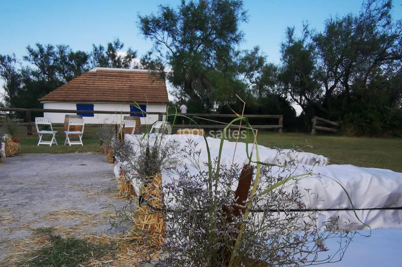Bottes de paille alignées en extérieur, entourées de végétation, avec une petite maison blanche en arrière-plan.