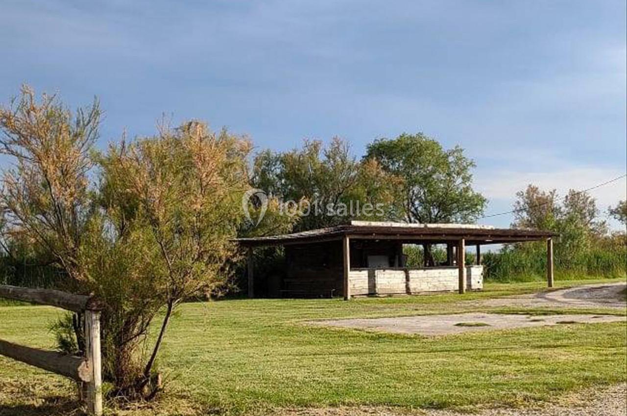 Abri en bois avec toit plat entouré de végétation, situé dans un espace ouvert avec une clôture en bois au premier plan.