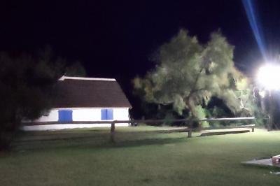 Maison blanche aux volets bleus éclairée la nuit, entourée d'arbres et d'une pelouse.