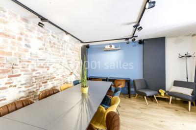 Salle de réunion moderne avec table noire, chaises, écran de projection, paperboard et cuisine ouverte en arrière-plan.