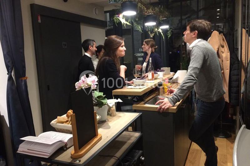 Des personnes discutent autour d'un comptoir dans un espace intérieur moderne et éclairé, avec des plantes suspendues.
