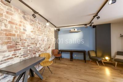 Salle de réunion moderne avec table noire, chaises, écran de projection, paperboard et cuisine ouverte en arrière-plan.