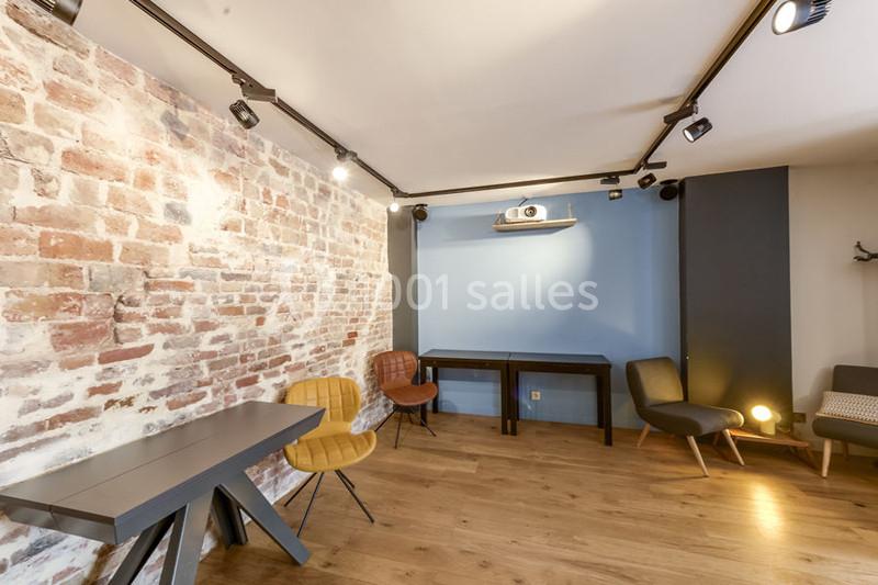 Salle lumineuse avec mur en briques, parquet, mobilier moderne et projecteur fixé au plafond.