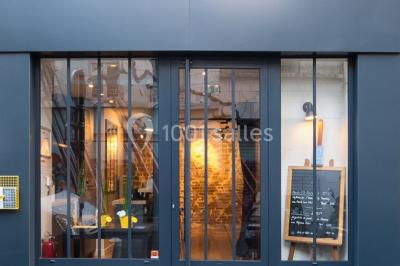 Salle de réunion moderne avec table noire, chaises, écran de projection, paperboard et cuisine ouverte en arrière-plan.