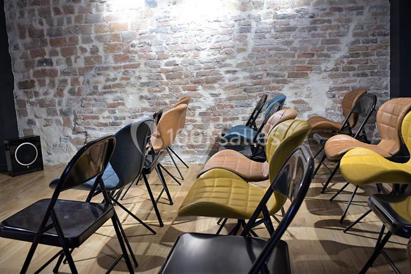 Chaises colorées disposées en rangées dans une salle avec un mur en briques apparentes.