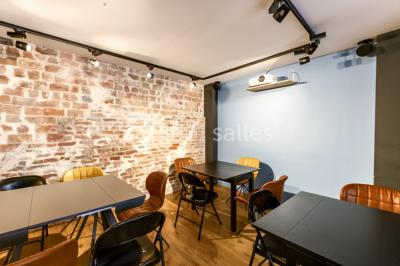 Salle de réunion moderne avec table noire, chaises, écran de projection, paperboard et cuisine ouverte en arrière-plan.