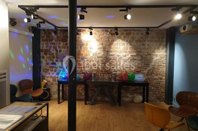 Salle de réunion moderne avec table noire, chaises, écran de projection, paperboard et cuisine ouverte en arrière-plan.