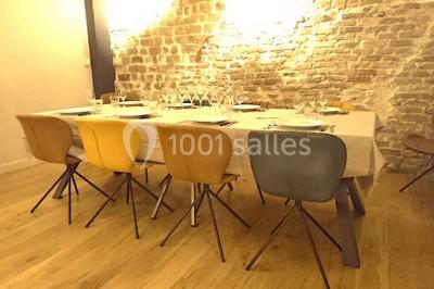 Salle de réunion moderne avec table noire, chaises, écran de projection, paperboard et cuisine ouverte en arrière-plan.