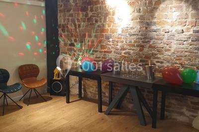 Salle de réunion moderne avec table noire, chaises, écran de projection, paperboard et cuisine ouverte en arrière-plan.