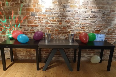 Salle de réunion moderne avec table noire, chaises, écran de projection, paperboard et cuisine ouverte en arrière-plan.