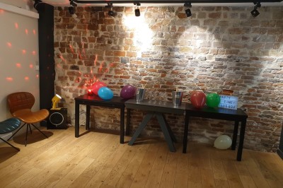 Salle de réunion moderne avec table noire, chaises, écran de projection, paperboard et cuisine ouverte en arrière-plan.