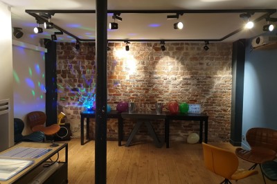 Salle de réunion moderne avec table noire, chaises, écran de projection, paperboard et cuisine ouverte en arrière-plan.