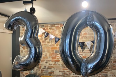 Salle de réunion moderne avec table noire, chaises, écran de projection, paperboard et cuisine ouverte en arrière-plan.