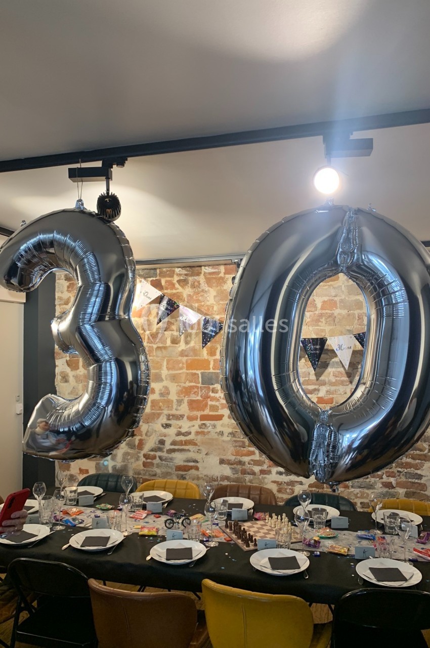Ballons argentés formant le chiffre 30 suspendus au-dessus d'une table décorée pour une fête dans une pièce en briques…