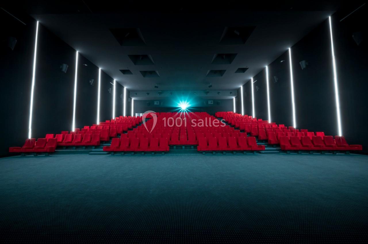 Salle de cinéma vide avec des rangées de sièges rouges et un projecteur allumé au fond.