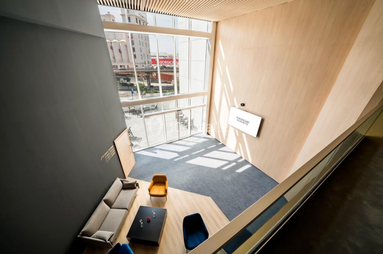 Vue intérieure d'un espace moderne avec canapé, fauteuils colorés, table basse et grande baie vitrée laissant entrer la…