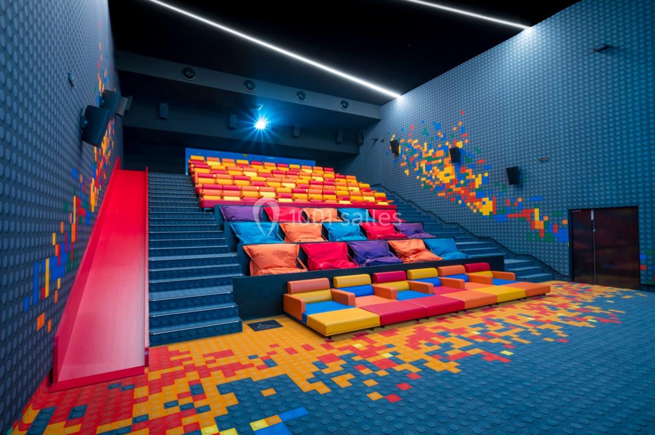 Salle de cinéma colorée avec gradins en coussins et sièges modulables, décorée de motifs pixelisés.
