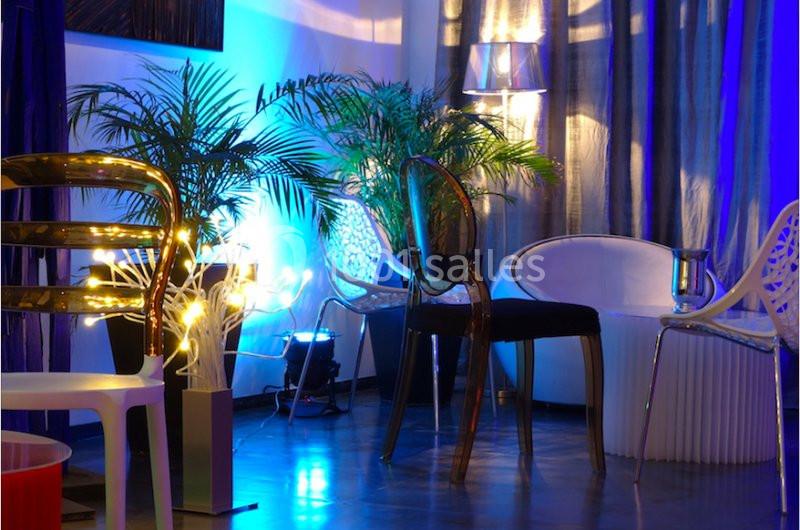 Espace intérieur moderne avec chaises design, plantes et éclairage d'ambiance bleu et jaune.