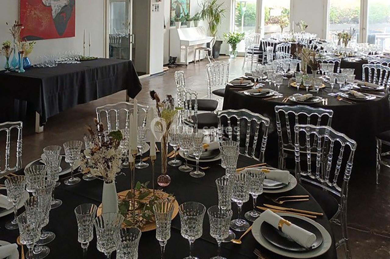Salle de réception élégamment dressée avec des tables rondes noires, des chaises transparentes et une décoration florale.