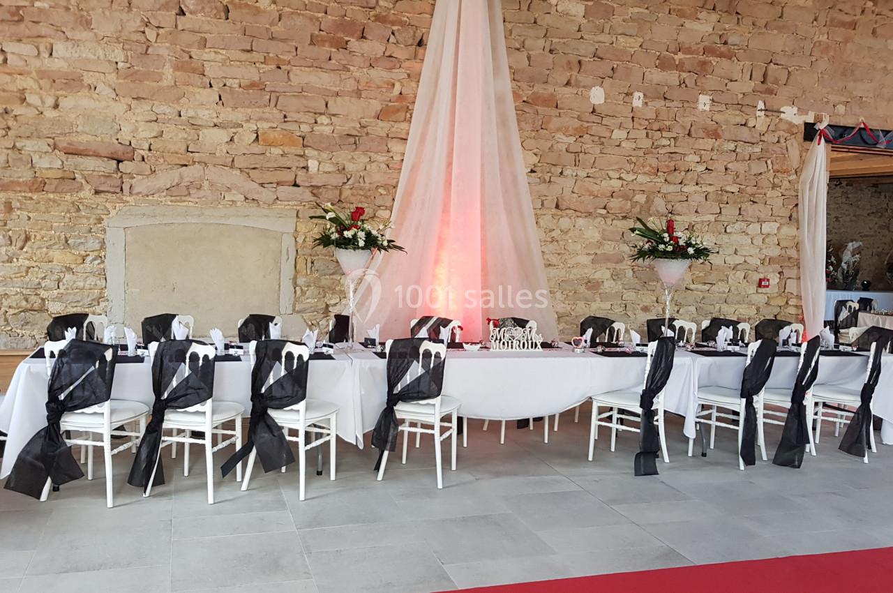 Salle de réception avec tables décorées de nappes blanches, chaises ornées de rubans noirs et murs en pierre apparente.
