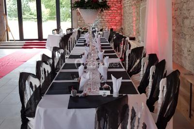 Cour d'une maison en pierre avec terrasse fleurie, arbres, guirlandes lumineuses et sol en gravier.