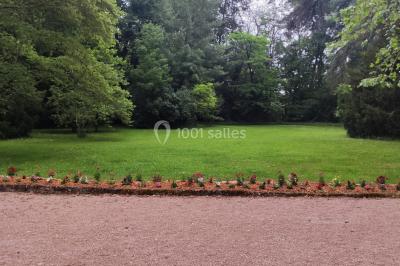 Cour d'une maison en pierre avec terrasse fleurie, arbres, guirlandes lumineuses et sol en gravier.