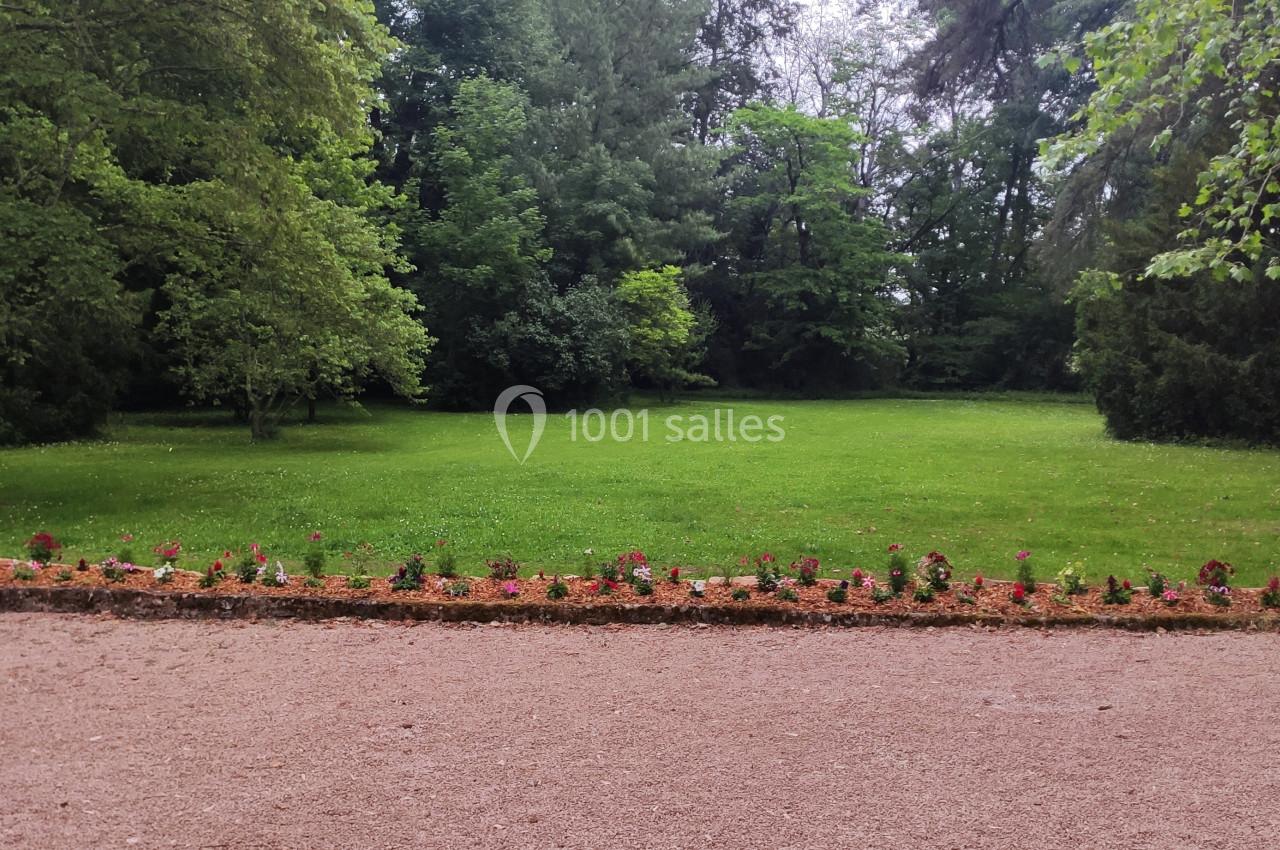 Pelouse verdoyante bordée d'arbres avec un parterre de fleurs colorées en premier plan.