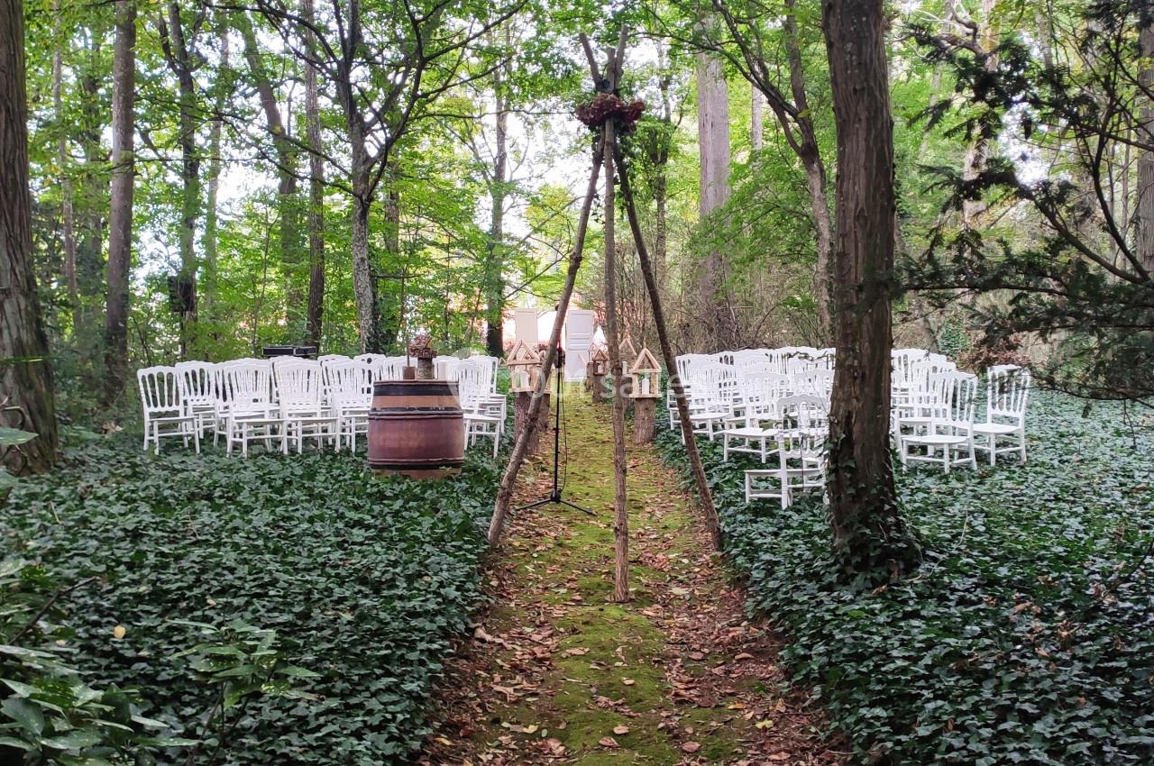 Chaises blanches disposées en rangées dans une clairière boisée, avec une allée centrale recouverte de mousse.