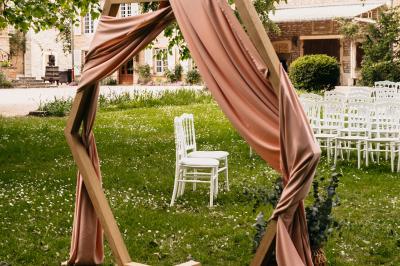 Cour d'une maison en pierre avec terrasse fleurie, arbres, guirlandes lumineuses et sol en gravier.