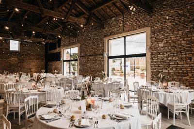 Cour d'une maison en pierre avec terrasse fleurie, arbres, guirlandes lumineuses et sol en gravier.
