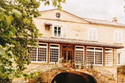 Cour d'une maison en pierre avec terrasse fleurie, arbres, guirlandes lumineuses et sol en gravier.