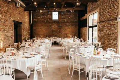 Cour d'une maison en pierre avec terrasse fleurie, arbres, guirlandes lumineuses et sol en gravier.