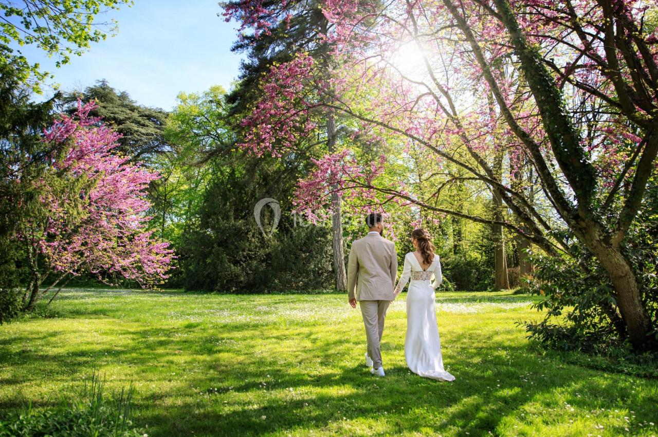 Un couple marche dans un jardin verdoyant entouré d'arbres en fleurs sous une lumière printanière.
