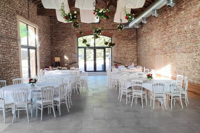 Cour d'une maison en pierre avec terrasse fleurie, arbres, guirlandes lumineuses et sol en gravier.