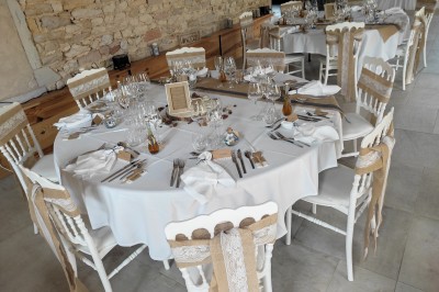 Cour d'une maison en pierre avec terrasse fleurie, arbres, guirlandes lumineuses et sol en gravier.