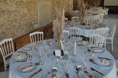 Cour d'une maison en pierre avec terrasse fleurie, arbres, guirlandes lumineuses et sol en gravier.
