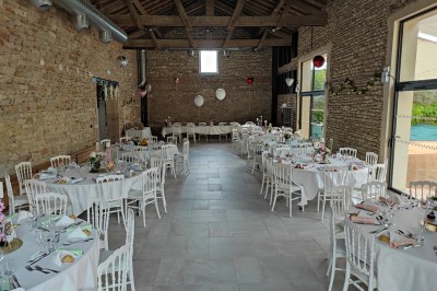 Cour d'une maison en pierre avec terrasse fleurie, arbres, guirlandes lumineuses et sol en gravier.