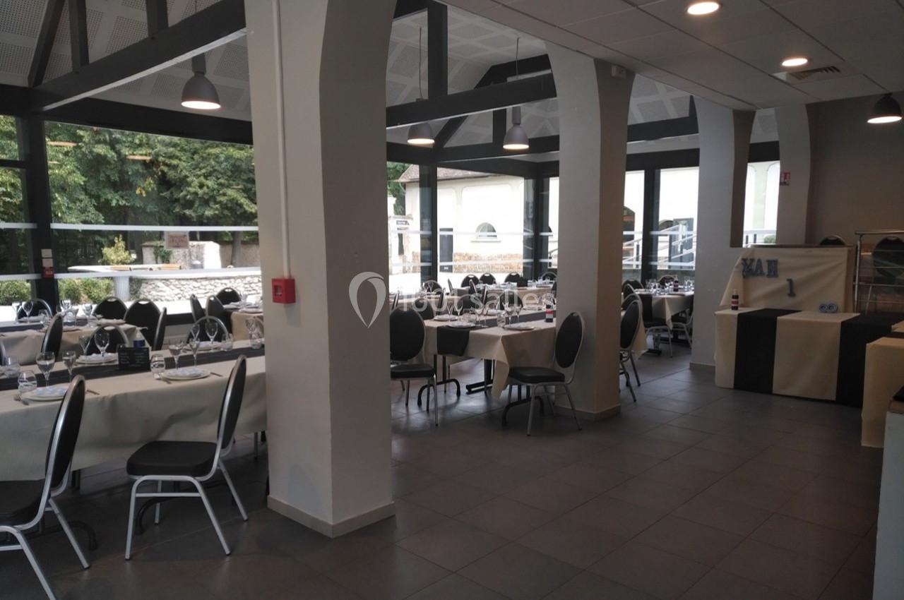 Salle de restaurant lumineuse avec tables dressées, chaises noires et grandes baies vitrées donnant sur un espace extérieur…