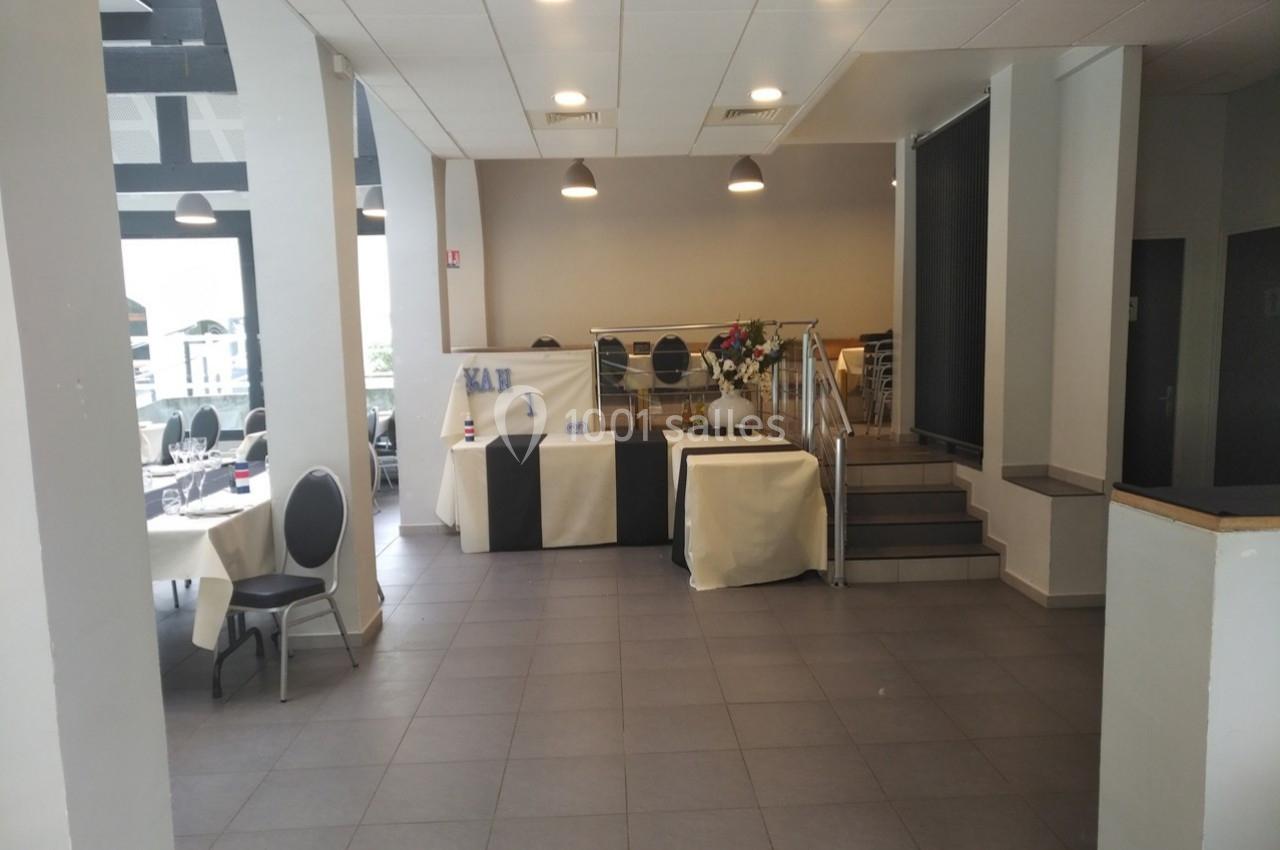 Salle de réception lumineuse avec tables dressées, escalier menant à une estrade et décoration sobre.