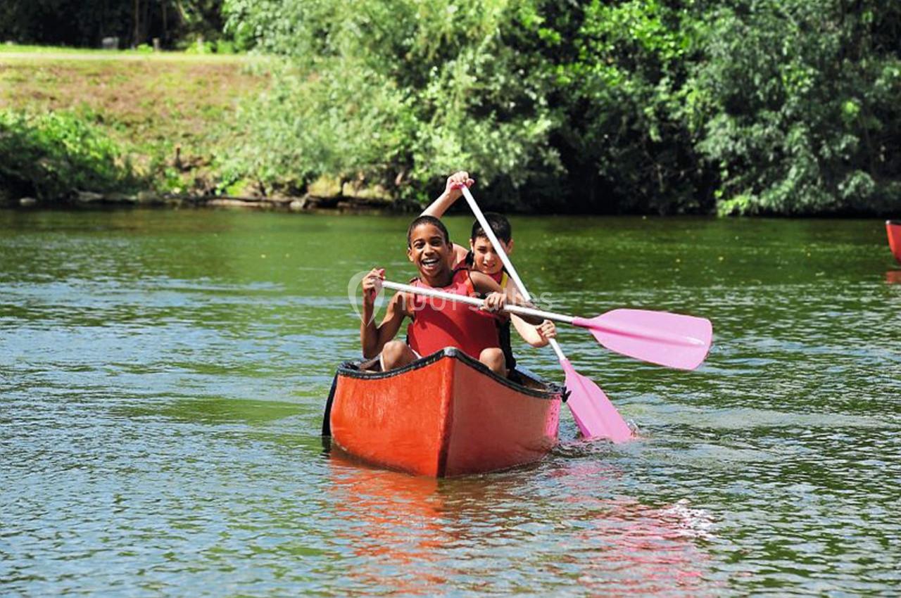 Deux personnes pagayant dans un canoë rouge sur une rivière entourée de végétation.