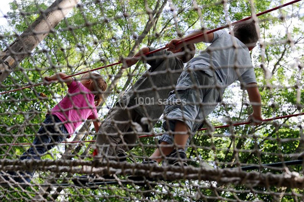 Des enfants traversent un pont de cordes suspendu dans une forêt, entourés de feuillage dense.