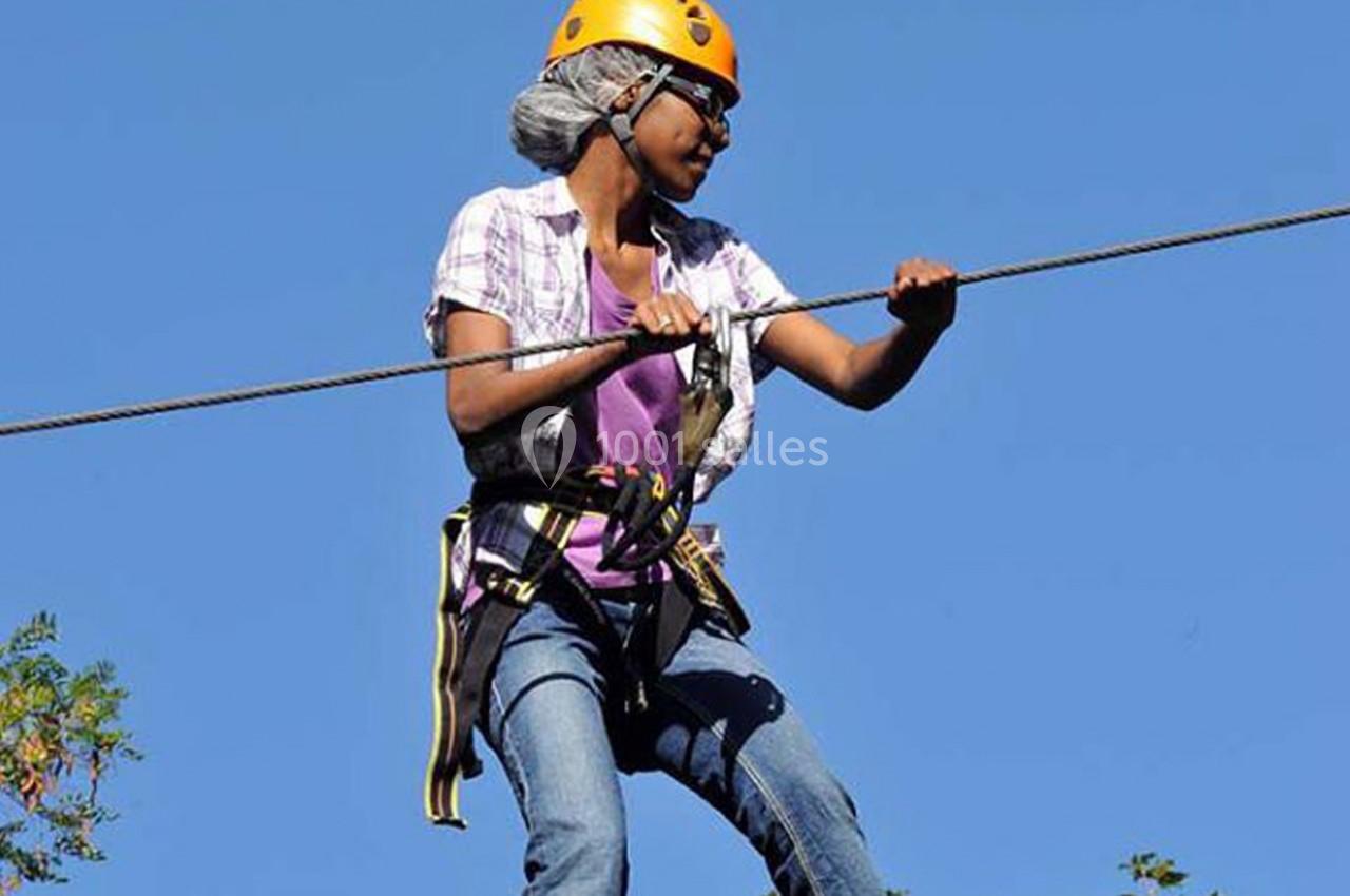 Une personne équipée d'un harnais et d'un casque traverse un parcours de tyrolienne sous un ciel dégagé.