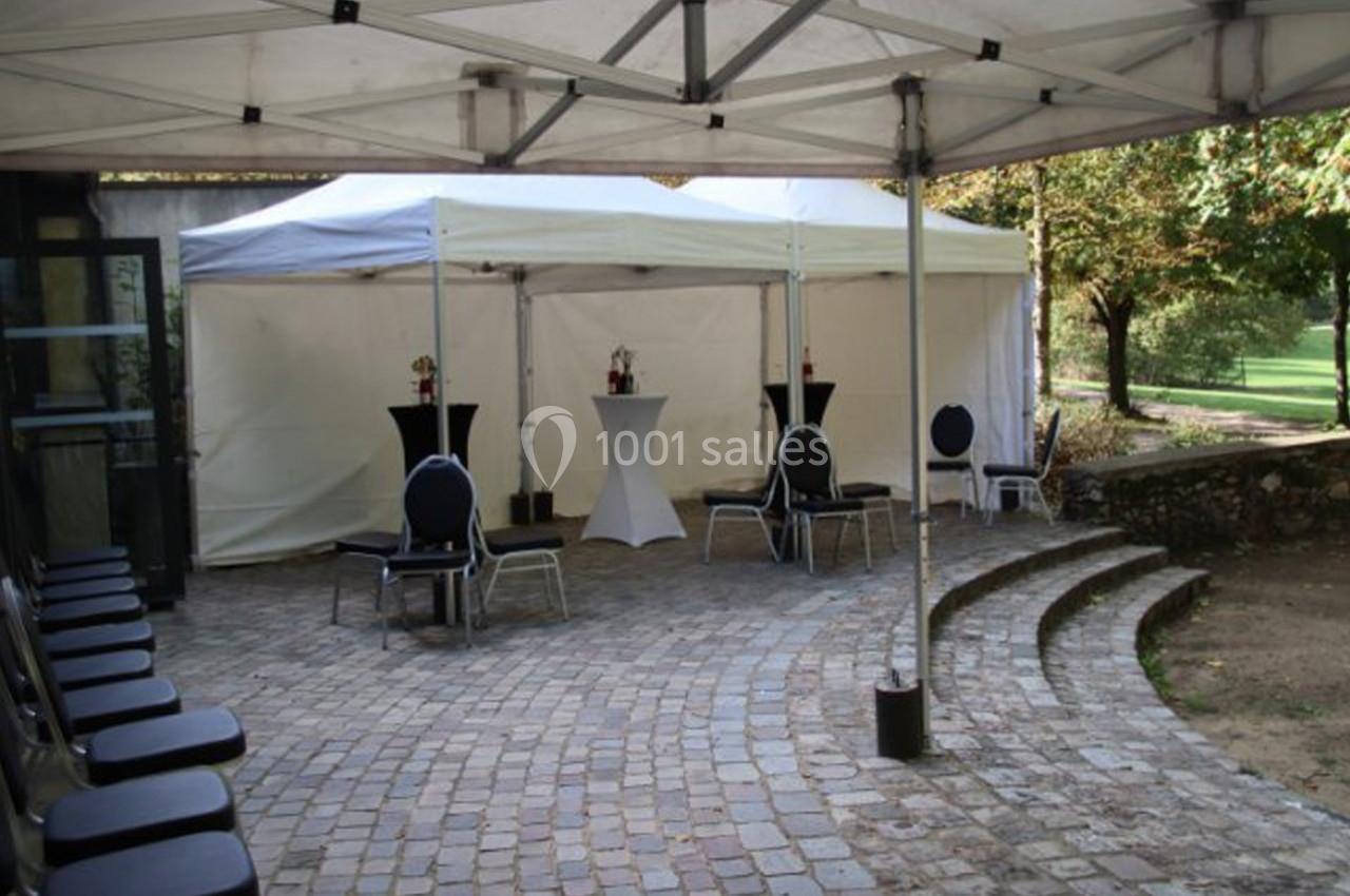 Espace extérieur avec pavés, chaises alignées et tentes blanches équipées de tables hautes pour un événement.